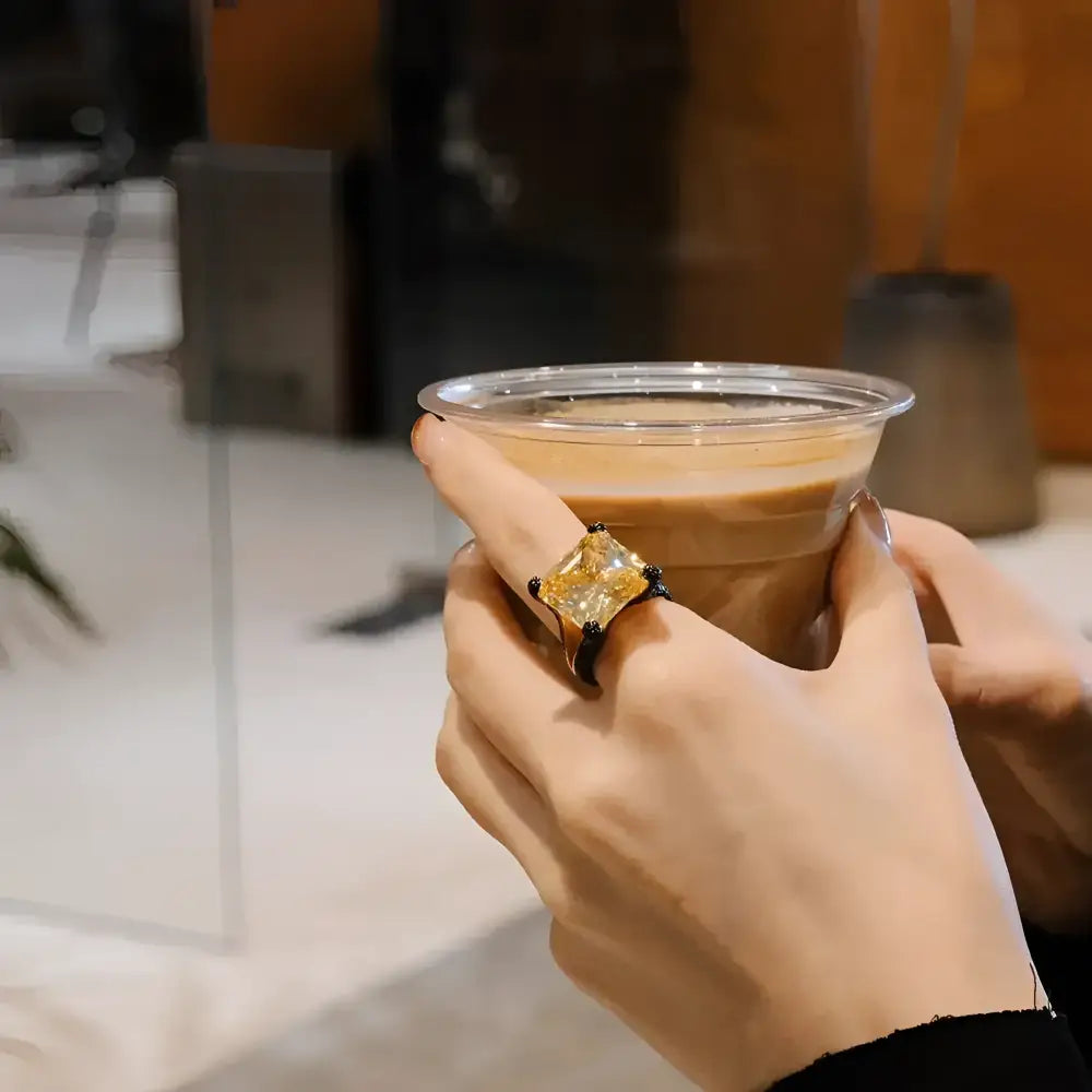 Coffee in a clear plastic cup with a large yellow gemstone ring.