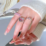 Hand adorned with pink-themed rings and glittery nails.