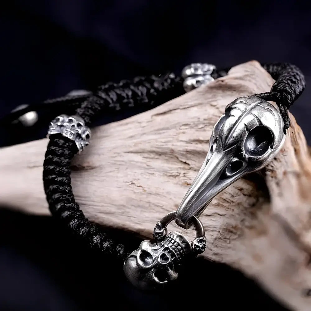 Black braided bracelet with silver skull and bird skull charms.