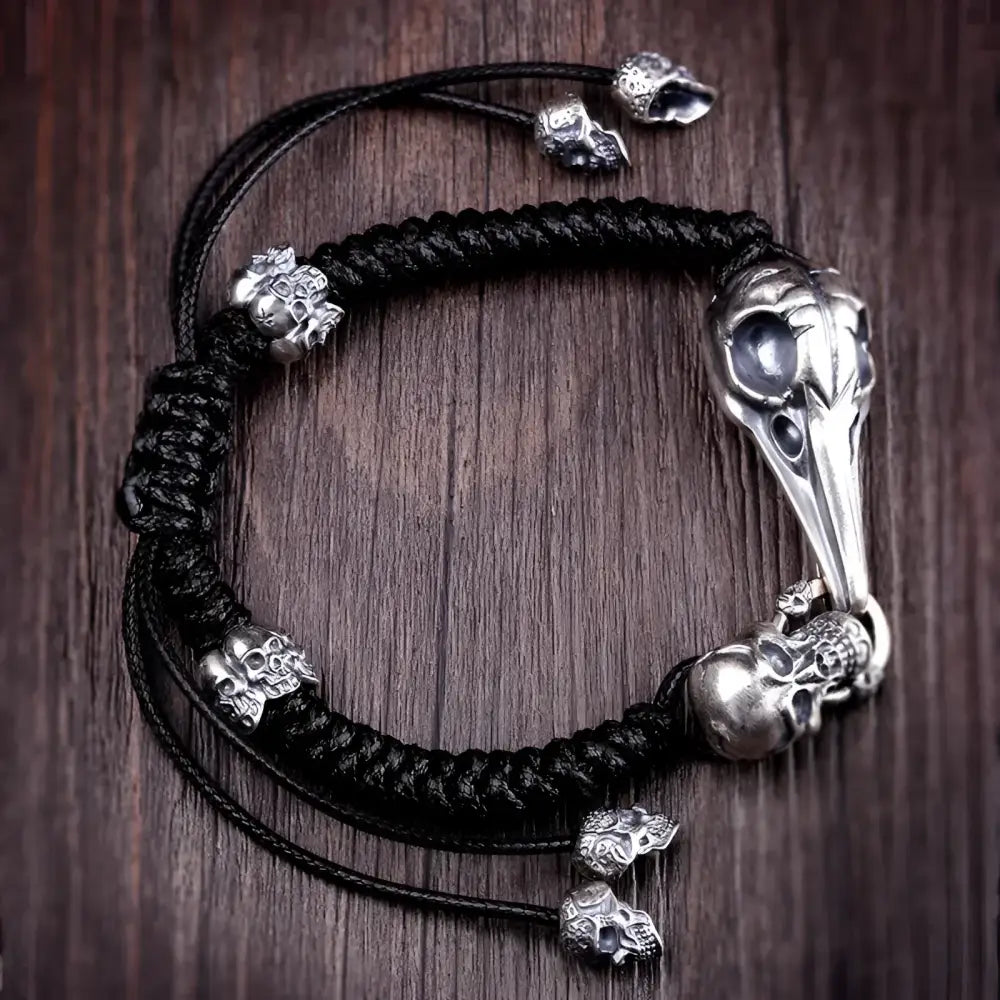 Black braided bracelet with silver skull and bird skull accents.