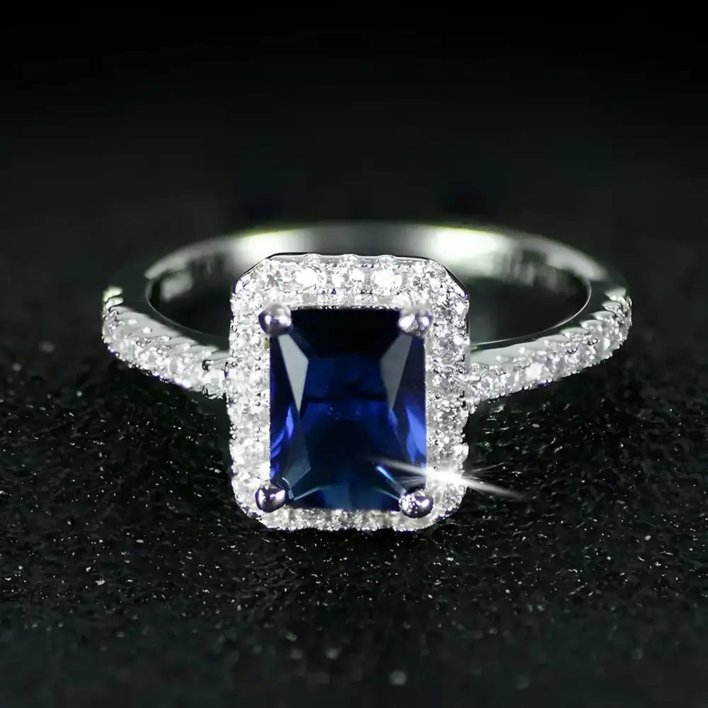 Silver ring with a rectangular blue gemstone surrounded by smaller diamonds.