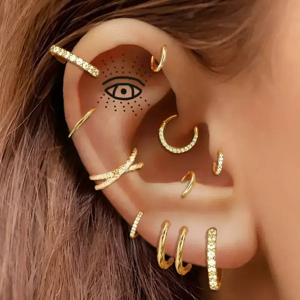 Ear with multiple gold earrings and an eye tattoo.